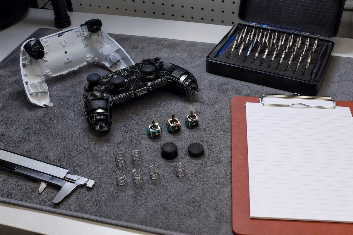 A controller partly disassembled on a workbench beside precision screwdrivers and a notebook of input timings